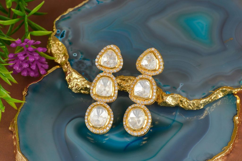 Close-up of luxurious diamond-studded gold earrings on a vibrant blue agate stone background.