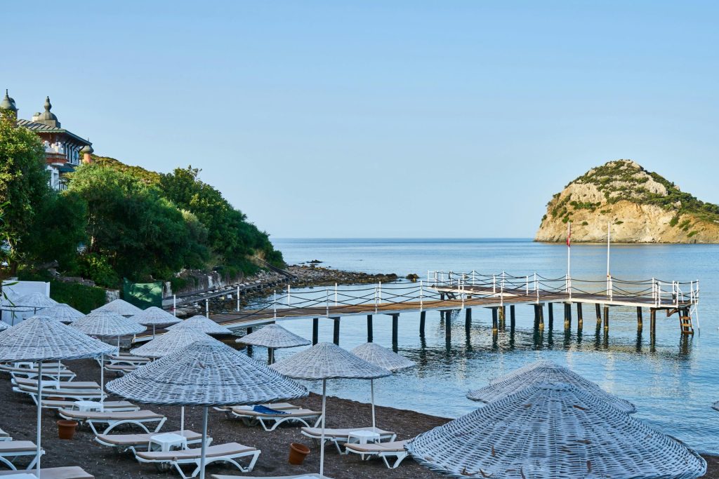 Serene coastal view with empty loungers, straw umbrellas, and a peaceful pier extending into the sea.