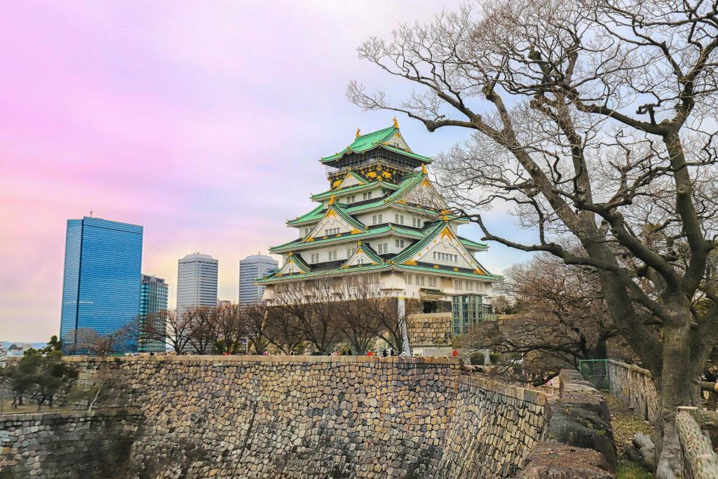 A captivating view of Osaka Castle with city skyscrapers and leafless trees in the foreground.