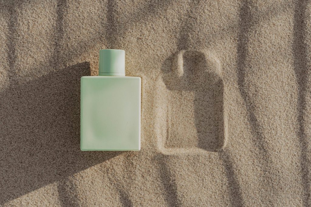 A green perfume bottle resting on sand, casting a shadow. Perfect for summer fragrance marketing.