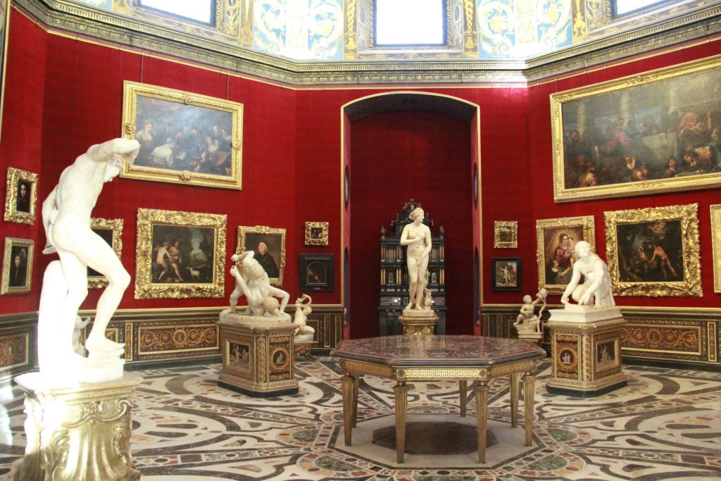 Sculptures and paintings displayed in a red gallery room.
